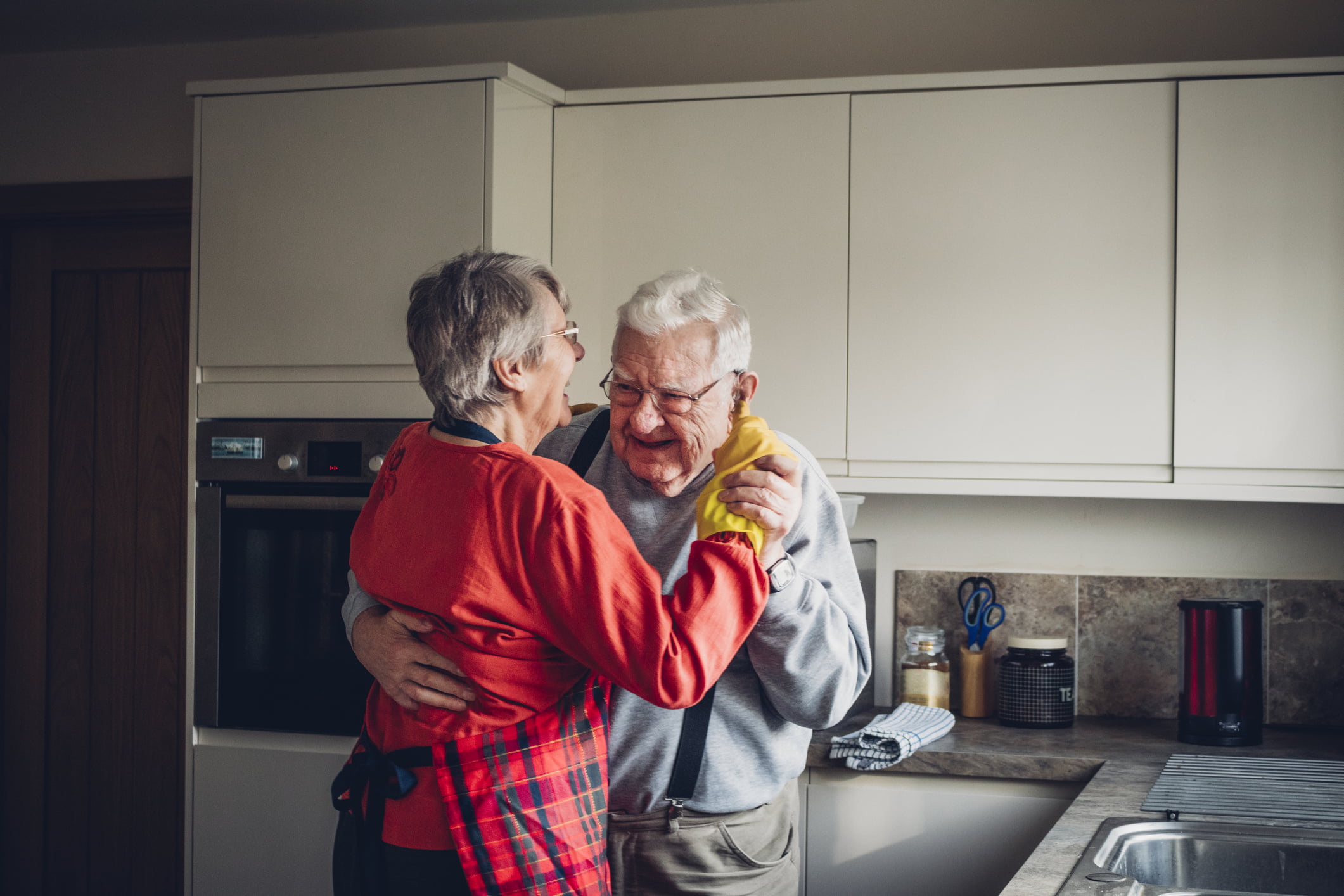 The senior couple dance in their kitchen.