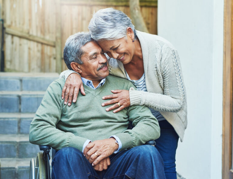 A cheerful elderly man seated in a wheelchair with his caregiver